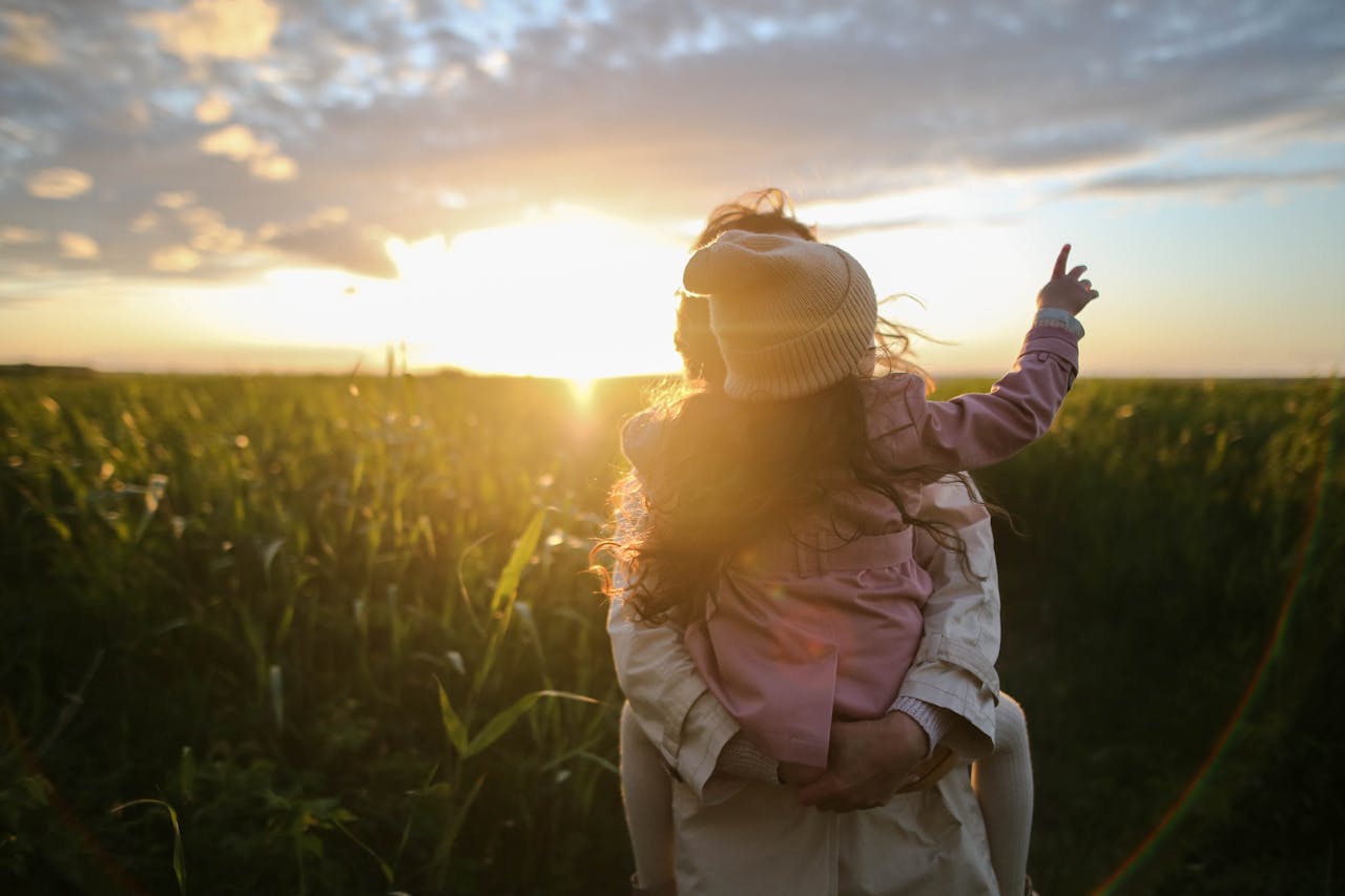 Mastering the First Impression: Your intriguing post title goes here A mother and daughter embrace and point at the sunset in a grassy field.