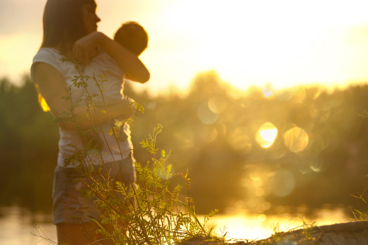 Home A serene moment of a mother holding her baby at sunset by a lake.